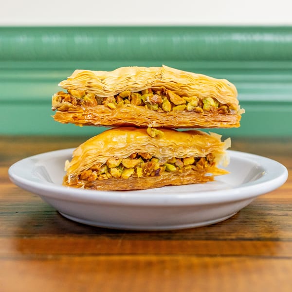 Two pieces of golden baklava with pistachio filling, stacked on a white plate.