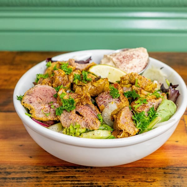 Mediterranean lamb and chicken shawarma salad with hummus and lime in a white bowl.
