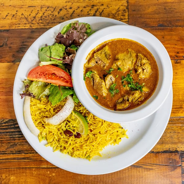 Mediterranean curry with rice, salad, and lime on a white plate, on a wooden table.