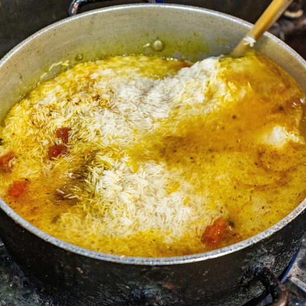 Rice and tomatoes cooking in a yellow broth in a large pot, stirred by a wooden spoon.