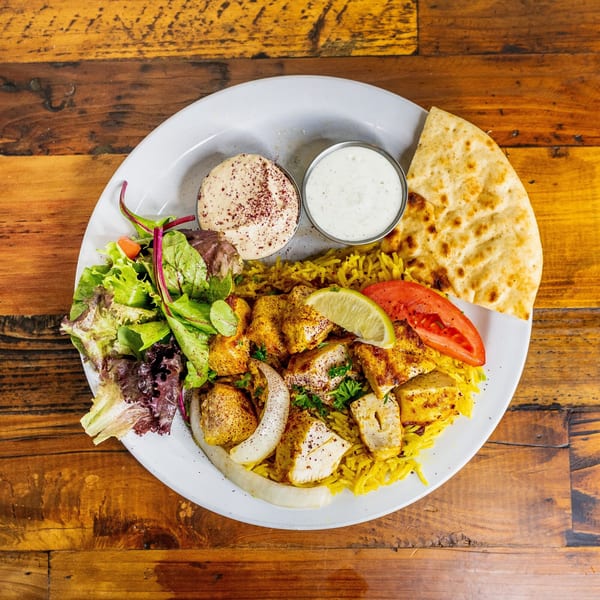Mediterranean chicken and rice platter with salad, hummus, tzatziki, and pita bread.