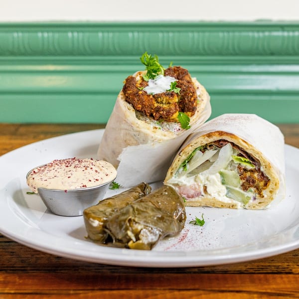 Two Mediterranean wraps, a side of dolmades, and a dipping sauce on a white plate.